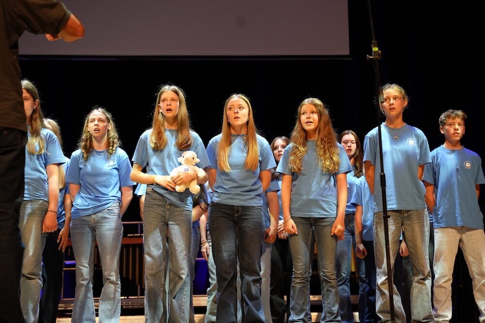 Singender Chor mit Stoffschaf in der Hand, Best of Schulwerk 2026