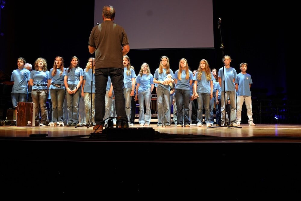 Schülerchor in Hellblau vor Mikrofonen, Best of Schulwerk Konzertbühne